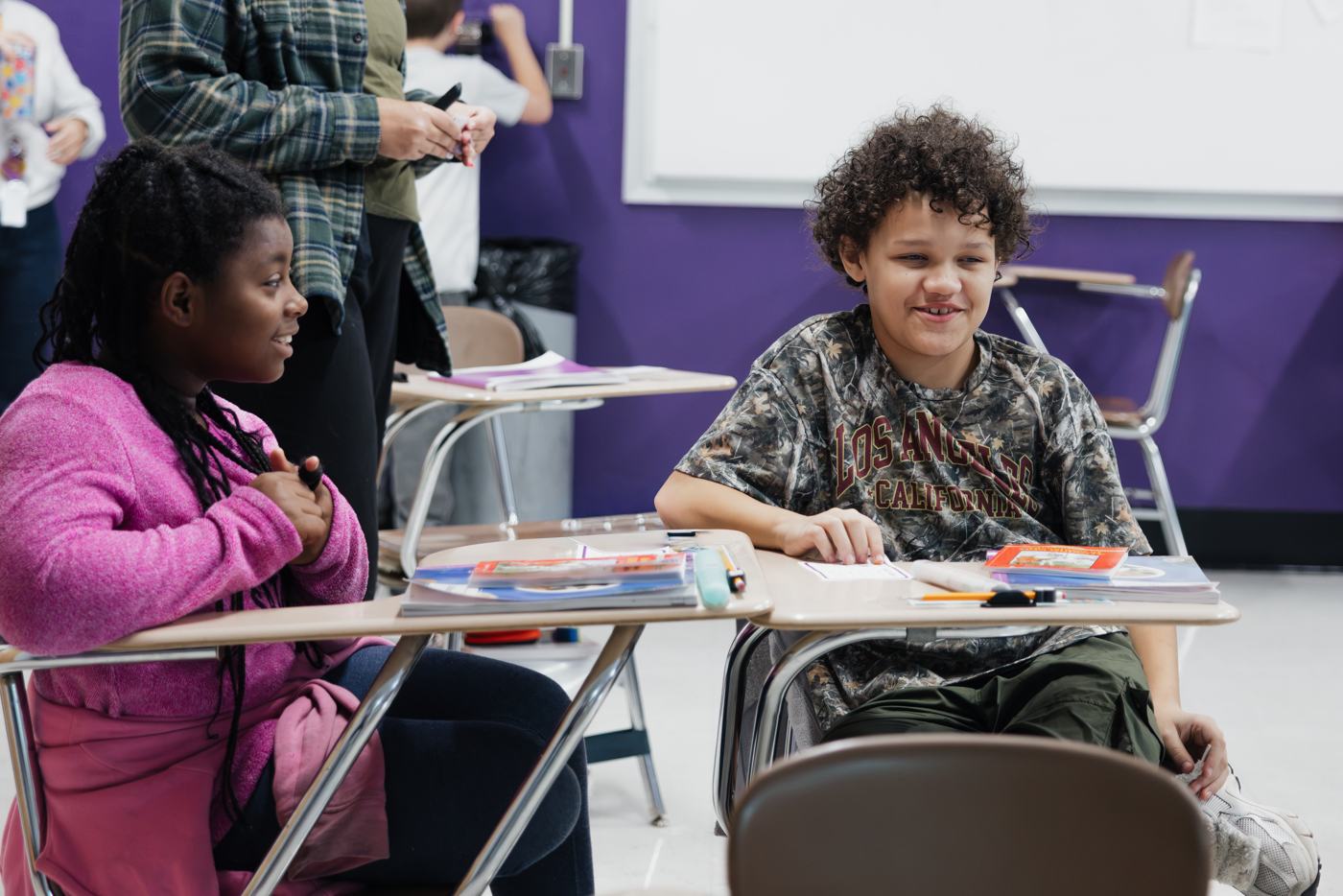 Two Marion students smile at their desks while listening to classmates share.